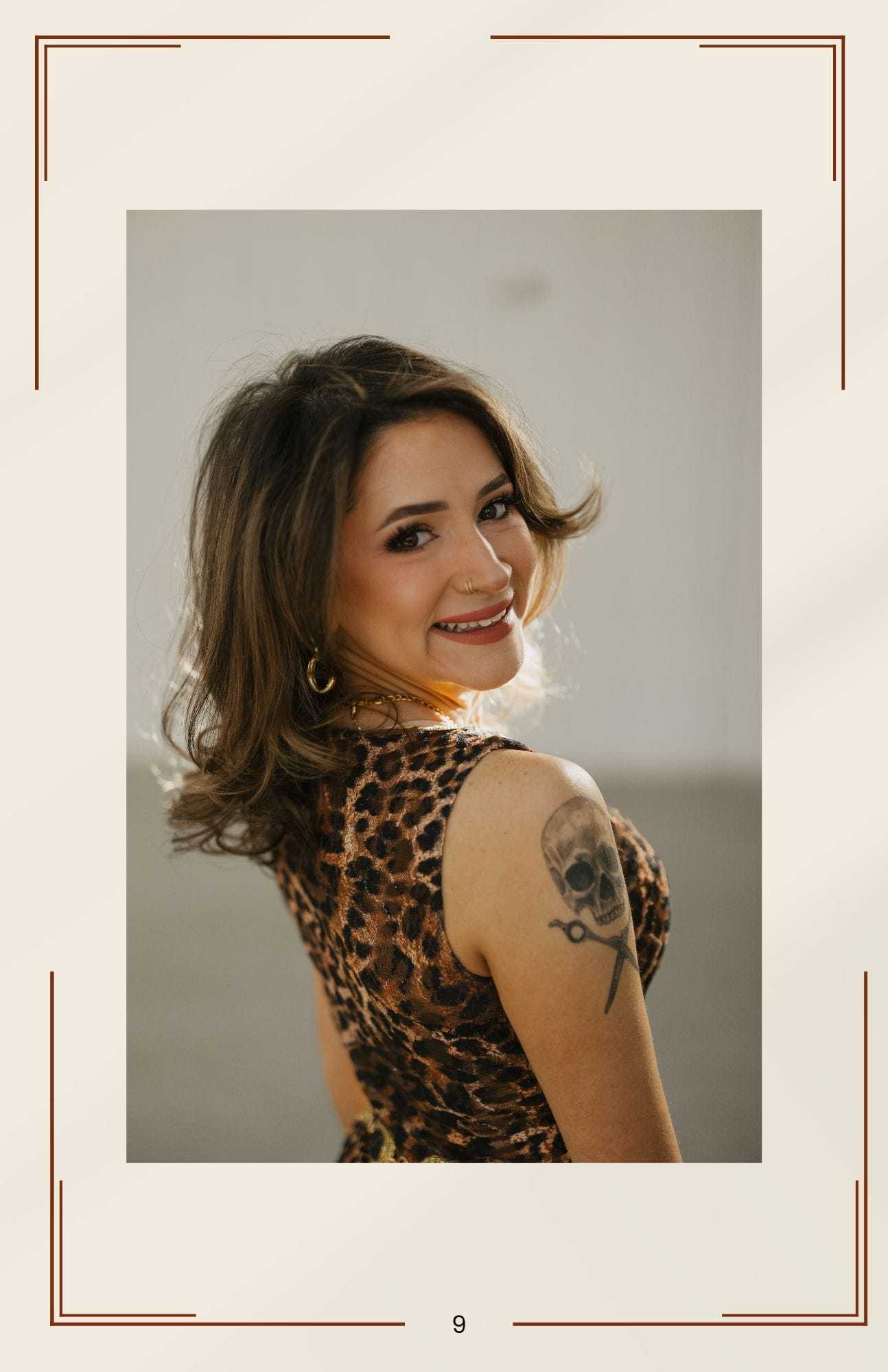 Smiling woman with leopard print dress and tattoo, posing confidently.