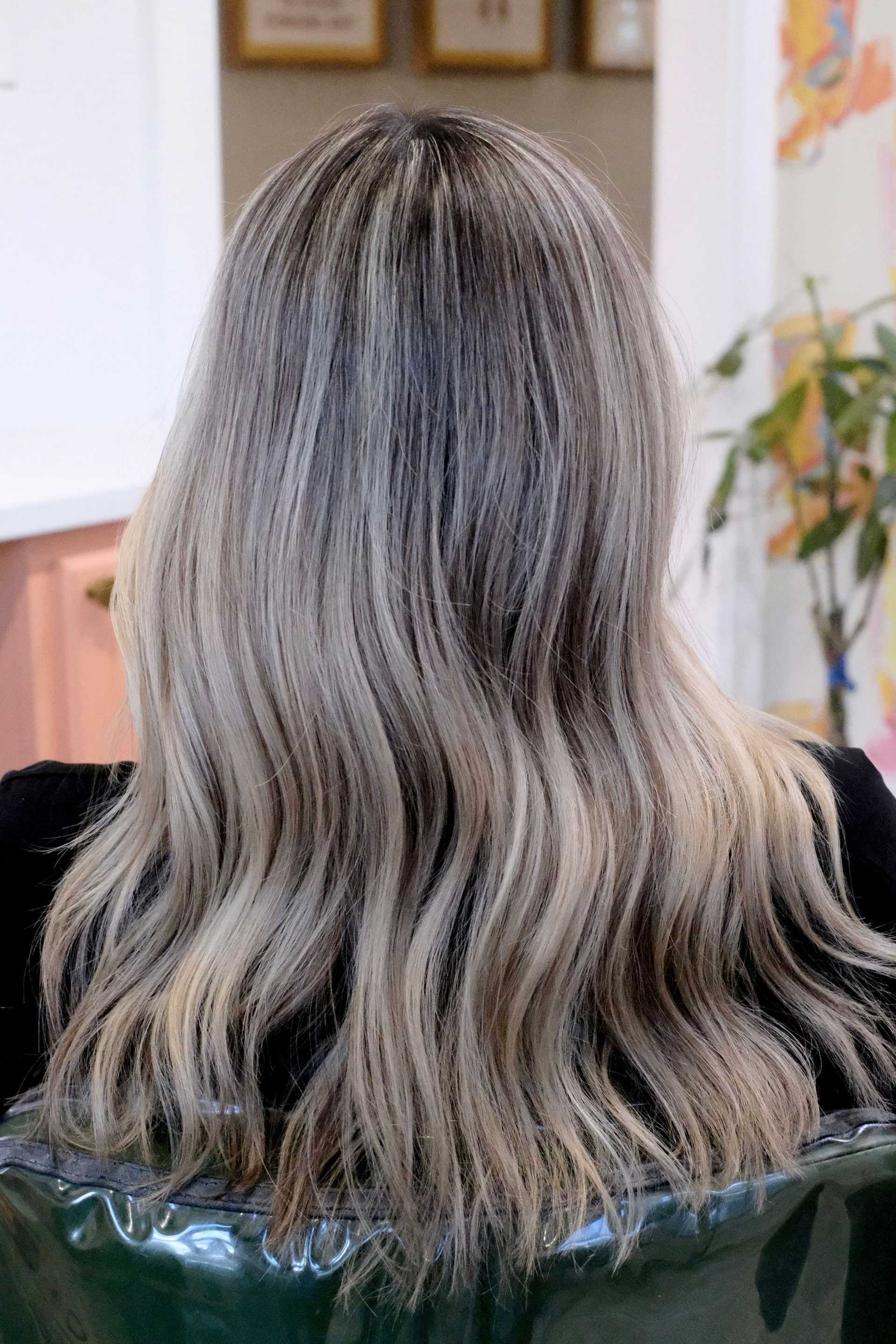 Long wavy hair styled in blonde shades, viewed from the back, in a salon setting.