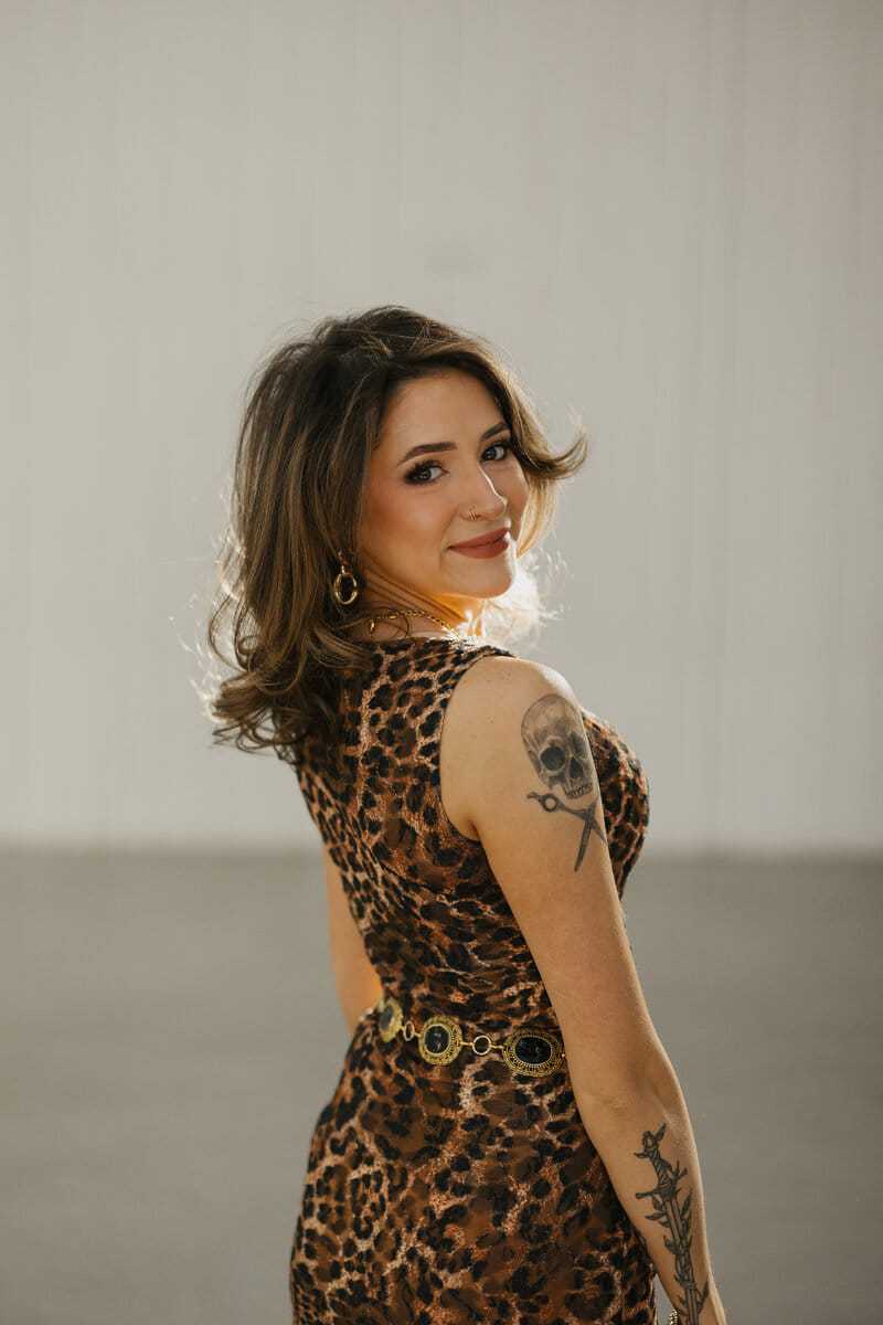 Woman in leopard print dress looking over shoulder with skull tattoo on arm.