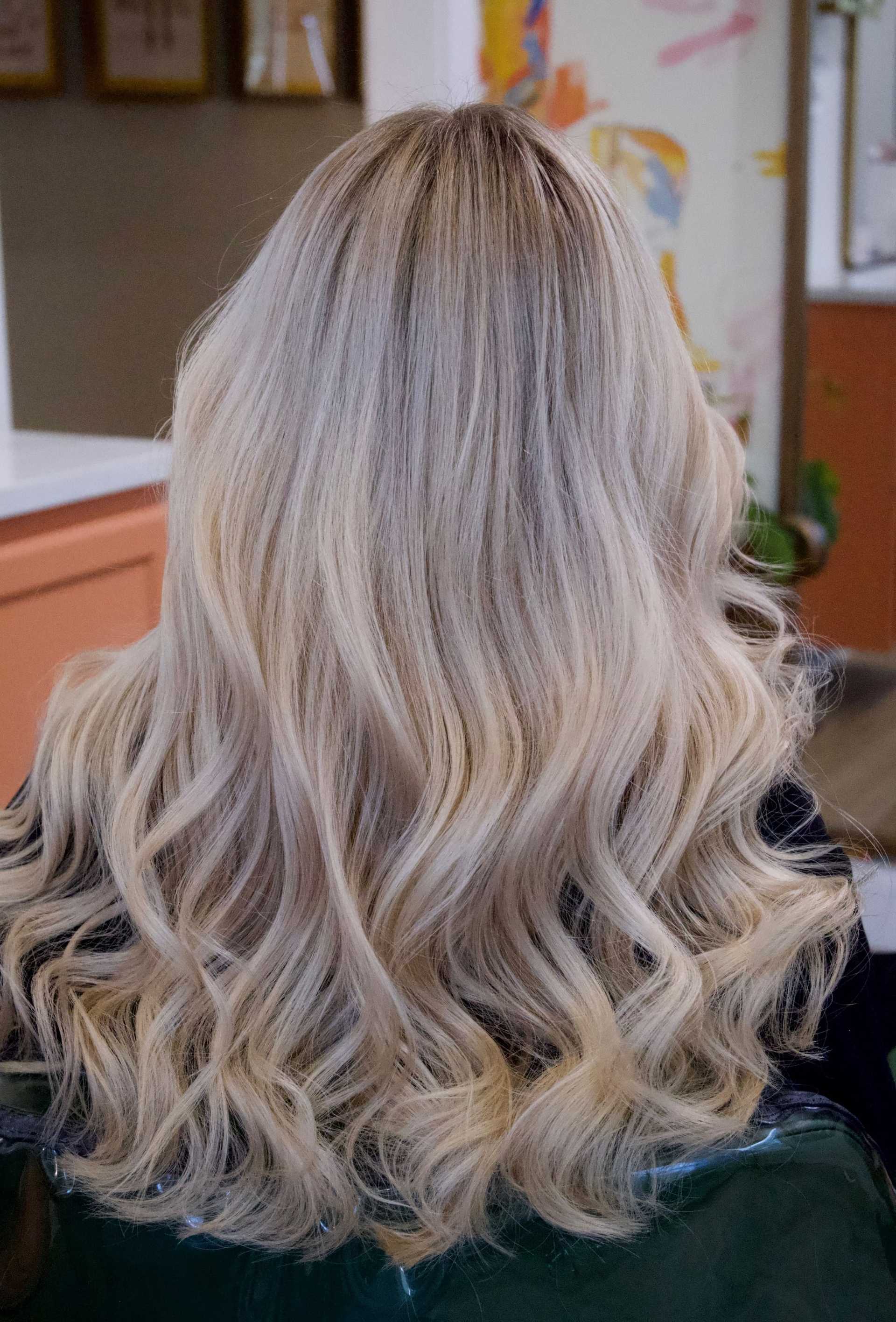 Long, wavy blonde hair shown from the back in a salon setting.